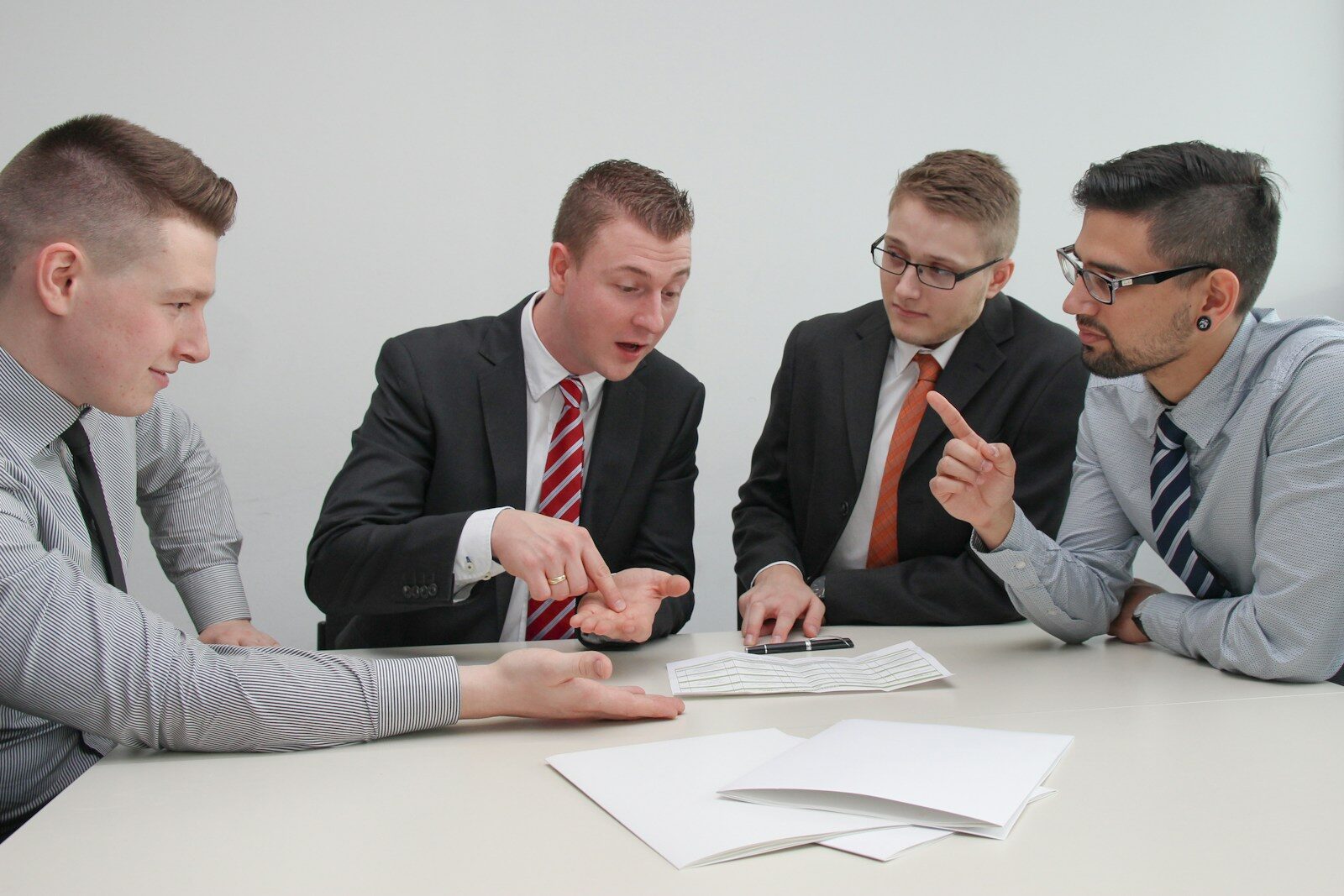four men sitting at desk talking relacionada a Processo administrativo parado: o que verificar primeiro