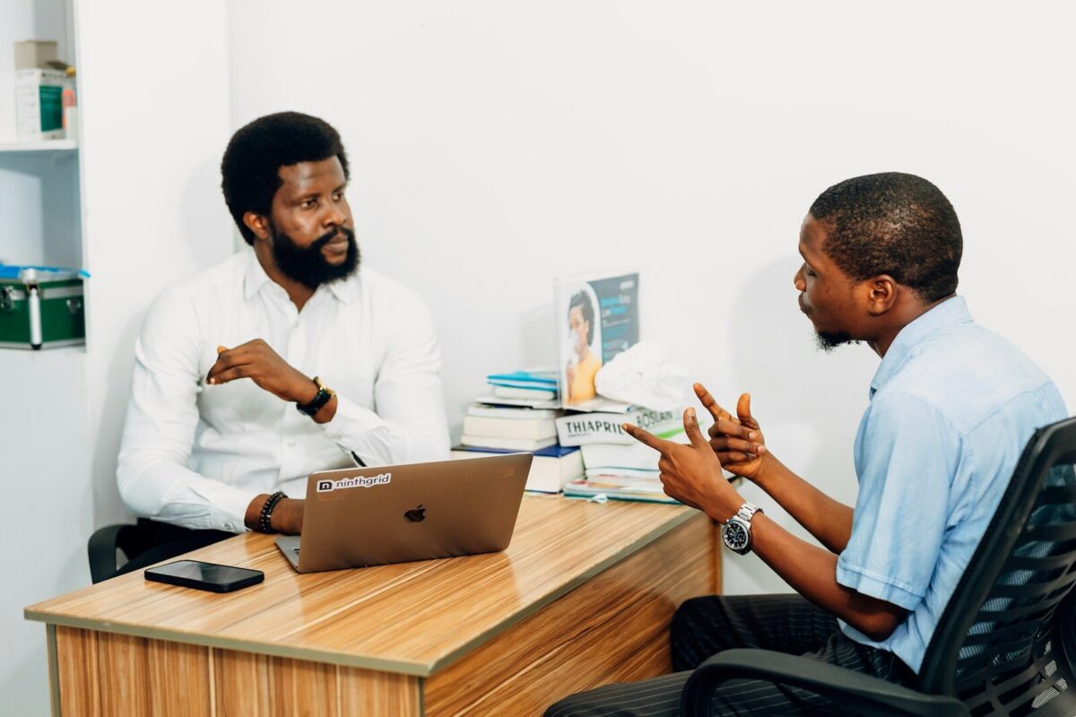 Two men sitting at a desk talking to each other